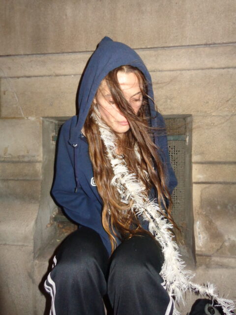 Singer Songwriter Sophia Stel wearing a navy blue hooded jacket and a white feather scarf. Her hair is partly covering her face